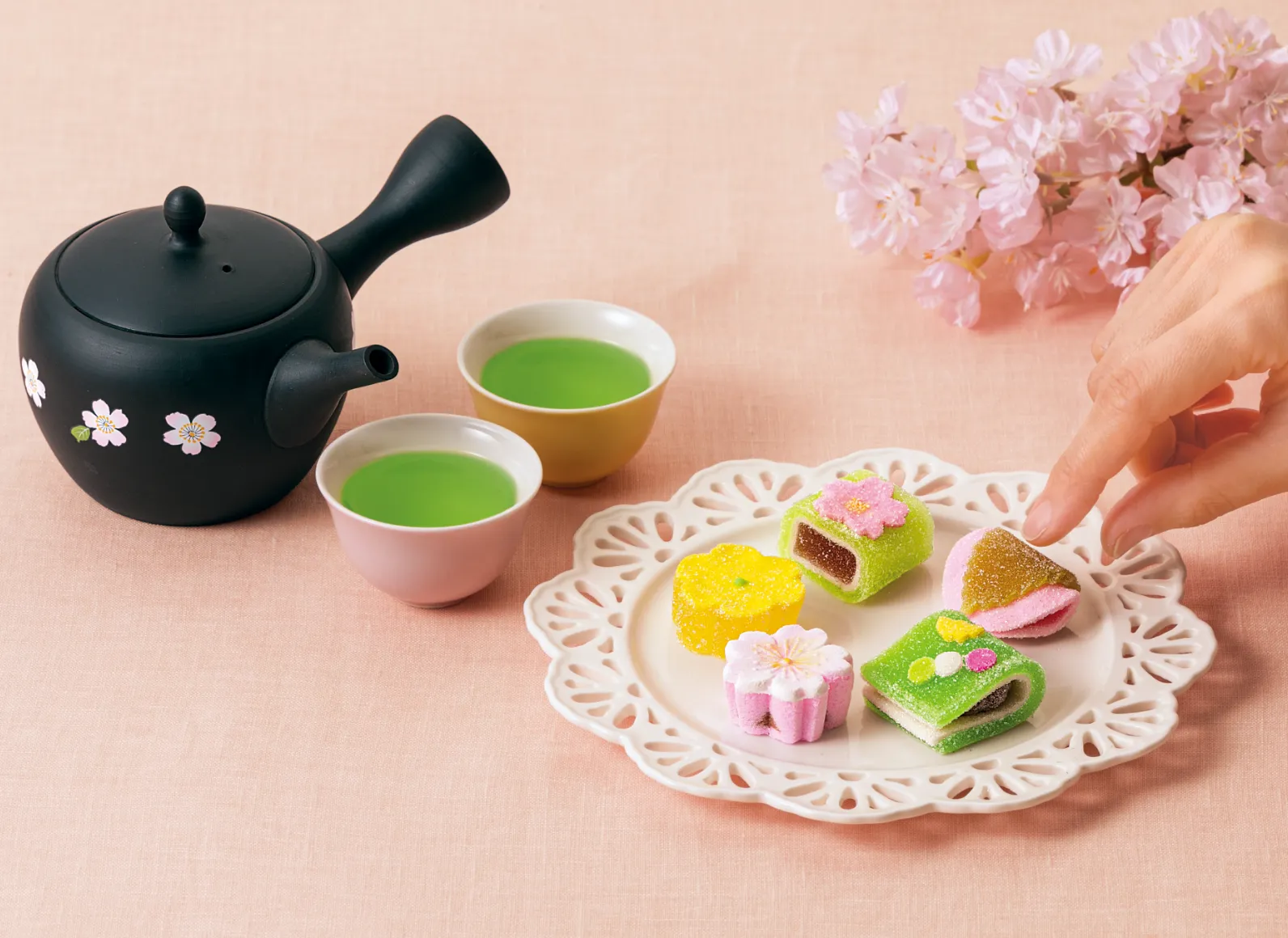 黒色の急須、お茶が注がれた二つの湯呑み、白色のお皿の上に並べられた細工菓子の画像