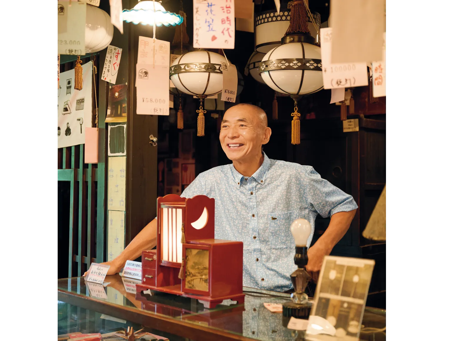 無数の照明がぶら下がったお店のカウンターに立つ佐藤成正さんの画像