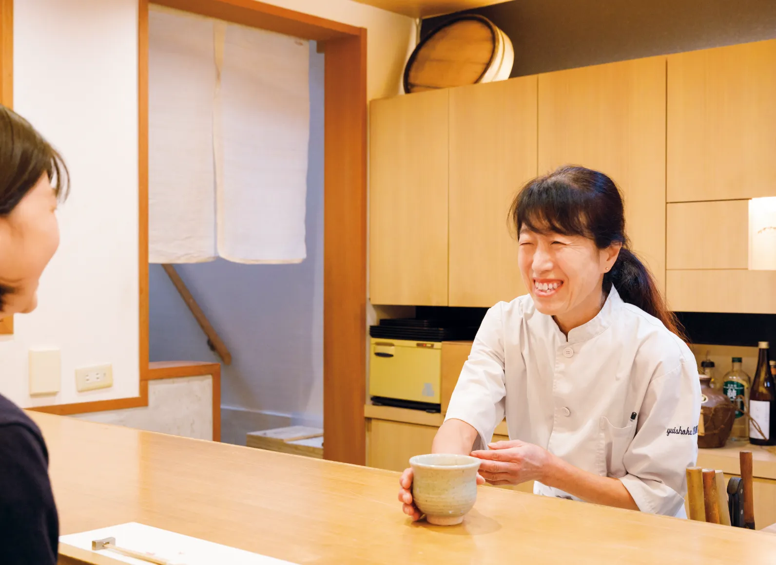 「唯食 いかわ」の店主、井川靖子さんが笑顔で湯呑みを差し出している画像