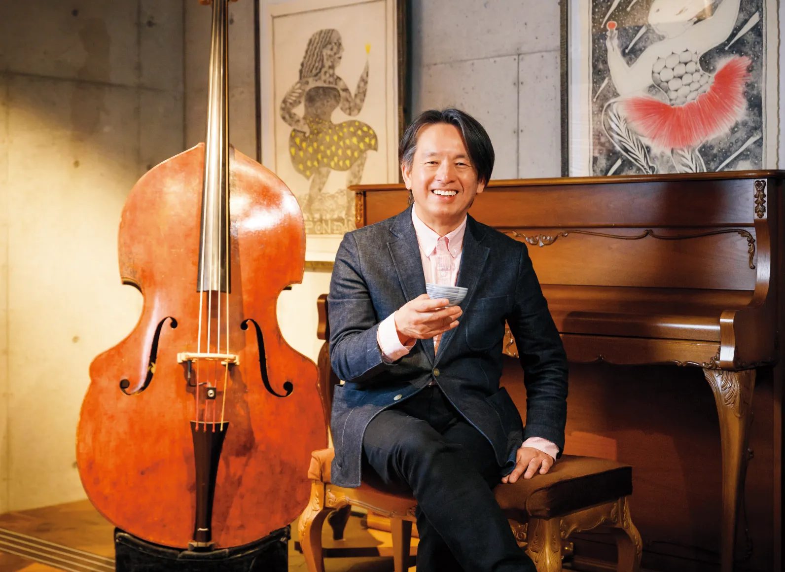 コントラバスの隣で、お茶を持って腰掛ける石田一夫さんの画像