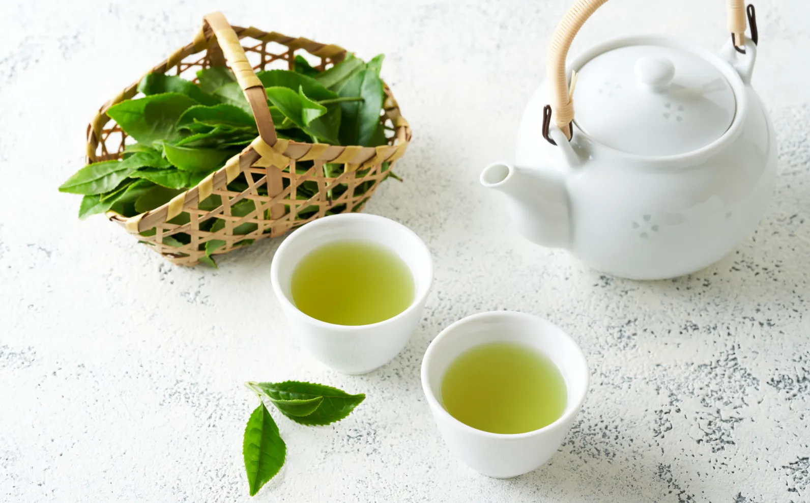 かごに入った茶葉、急須、お茶の入った二つの湯呑みの画像